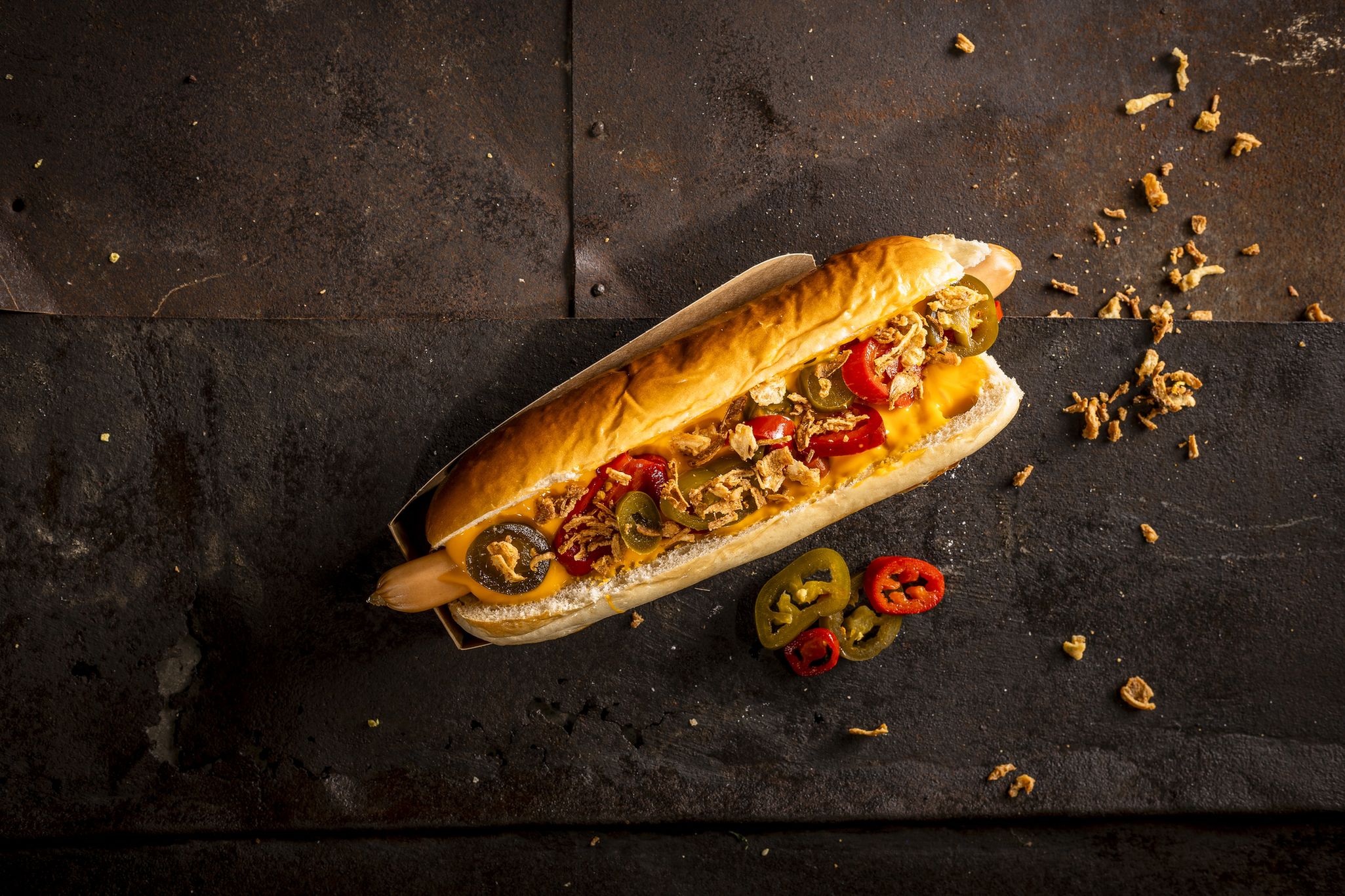 Ein belegtes hotdog mit paprika und jalapeños auf einem tisch.
