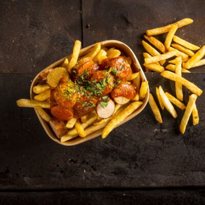 Ein teller mit pommes und currywurst auf einem holzuntergrund.