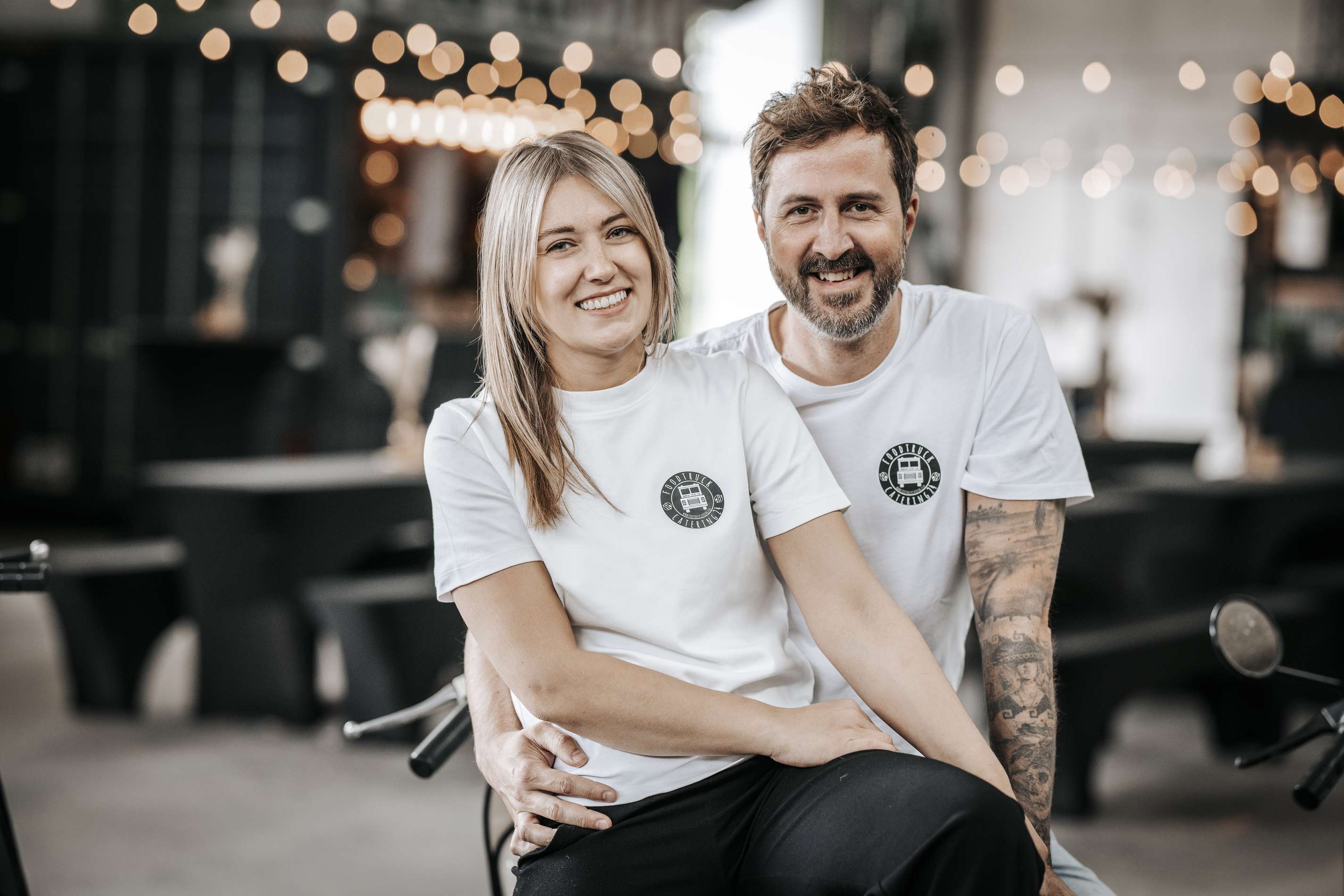 Ein laechelndes Paar in Foodtruck Catering24-Shirts sitzt zusammen.