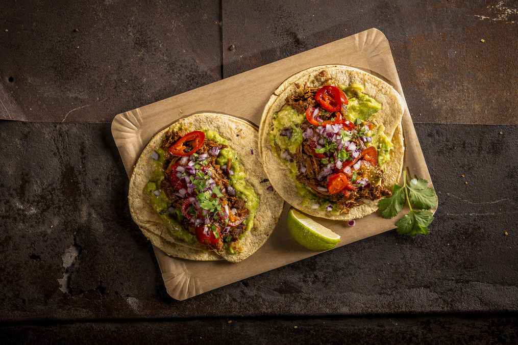Zwei mit frischen zutaten belegte tacos auf einem holzbrett.