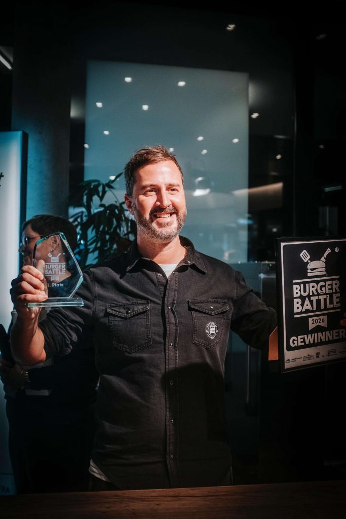 Ein Brauer zeigt stolz eine Urkunde und einen Bierkrug.