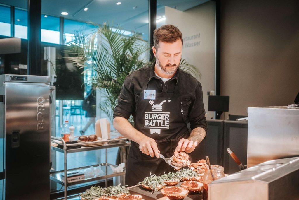 Ein Koch bereitet in einer modernen Kueche ein Gericht mit frischen Zutaten zu.